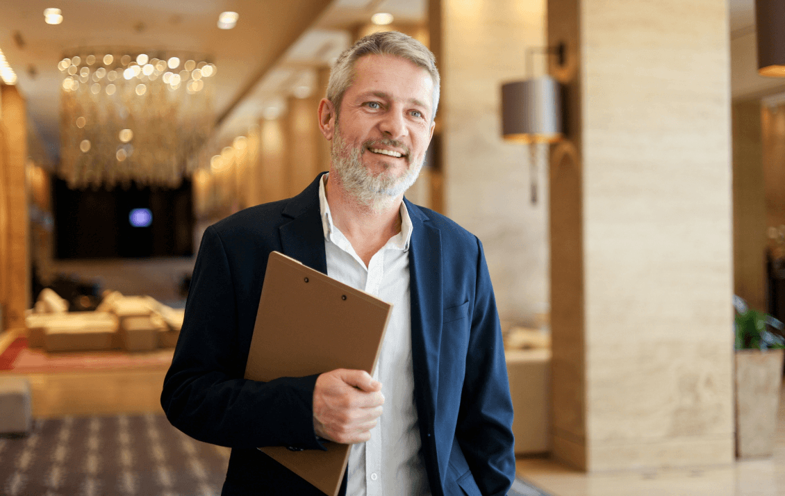 Hotel owner walking through a luxury hotel lobby holding a clipboard while overseeing operations and team performance