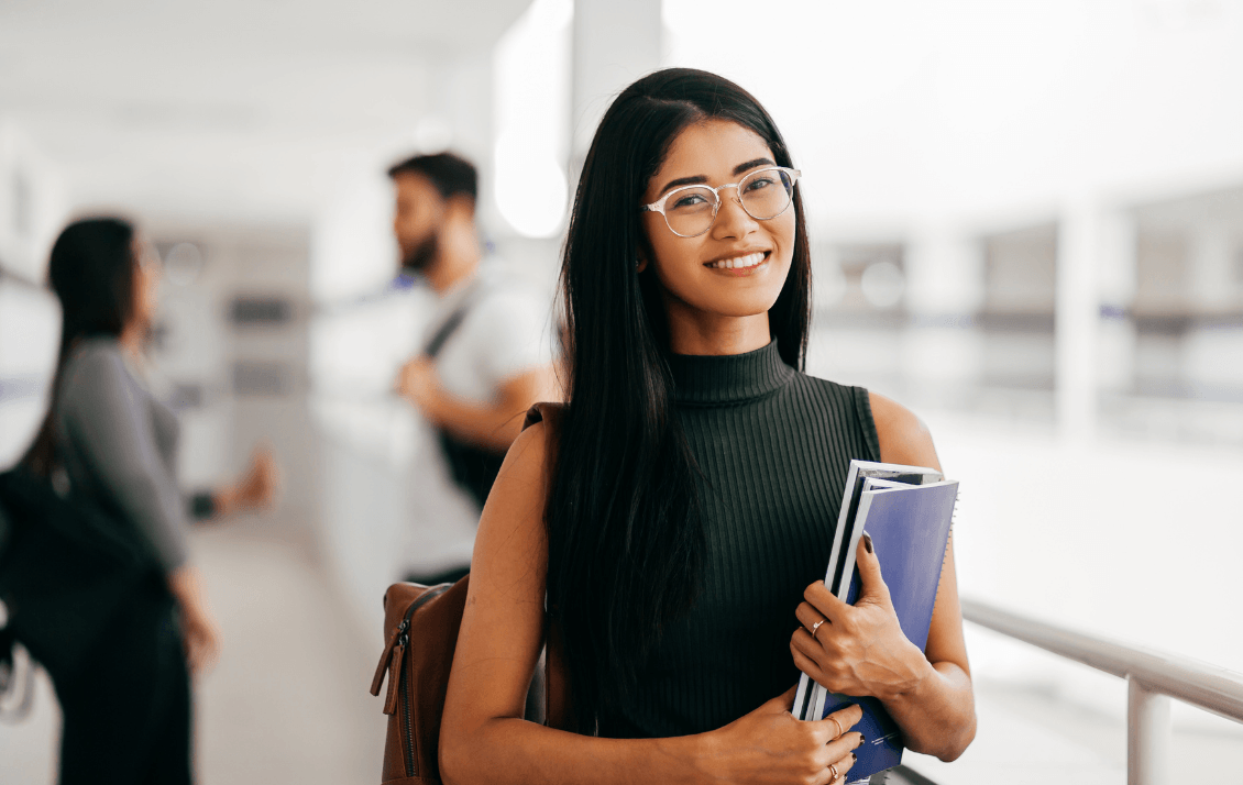 Hospitality student holding notebooks and smiling on campus