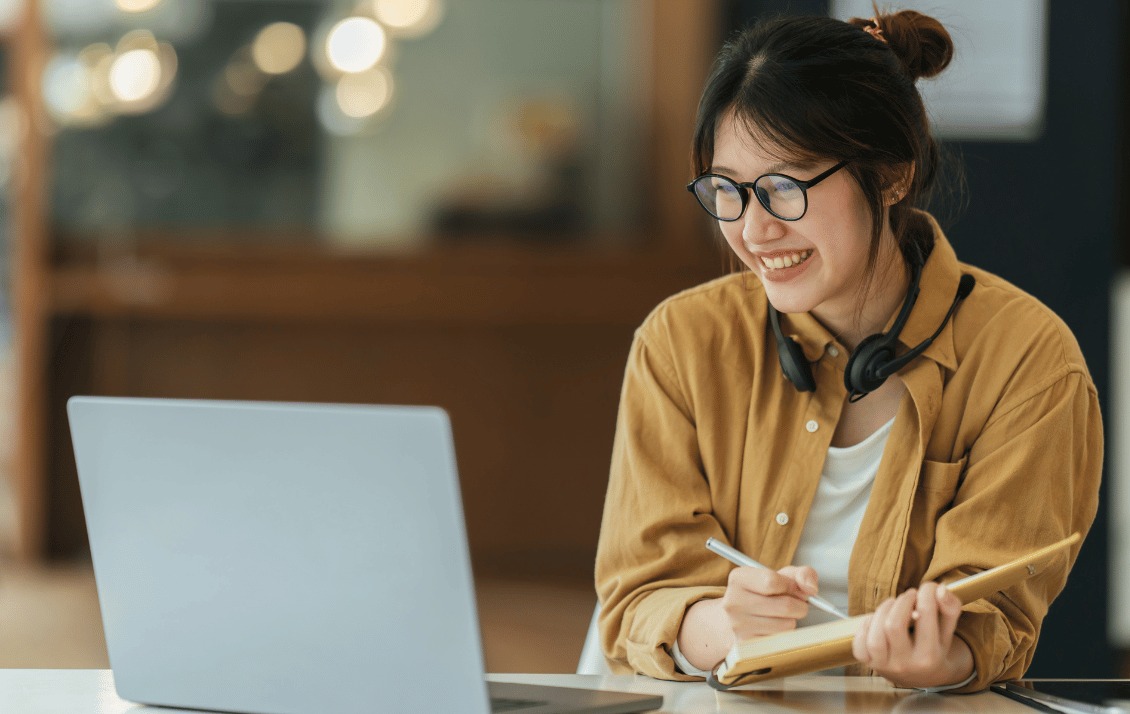 Hospitality student taking notes while watching a learning video and smiling on campus